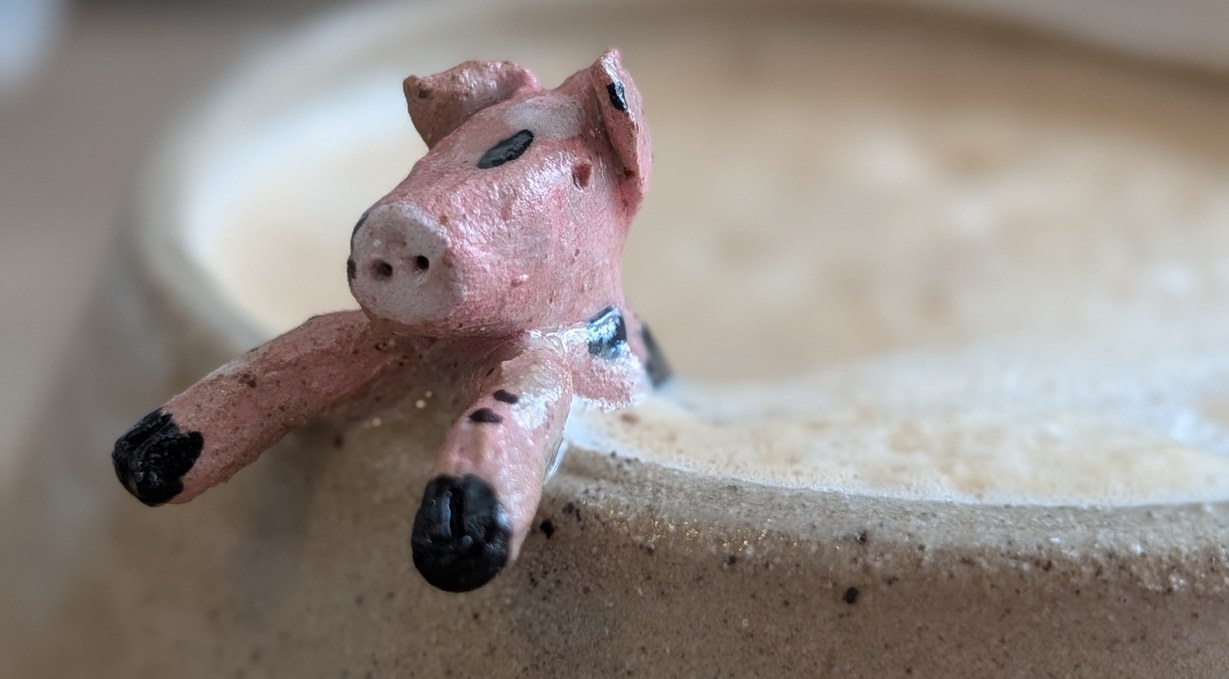 A small pink pig sculpture resting over the rim of a stoneware bowl