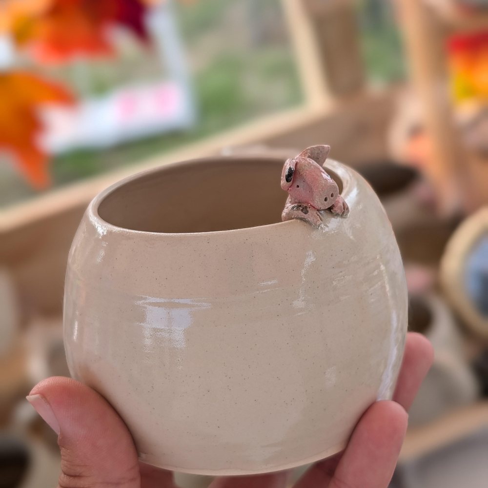 White clay mug with a pink pig hanging over the rim